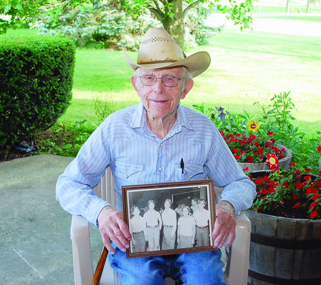Bob Peterson holds a picture of the first Supreme Showmanship contestants. From left: Terry (Quear) Boone, cattle; Beth (Lancaster) Moon, horses; Janet (Peterson) White, sheep; Marilyn Foland, pigs; and Johnny Roberts, dairy. (Photo by Robert Herrington)