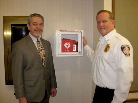 Kerry Green, Executive Director of the Hussey-Mayfield Public Library, and Steve Gilliam Division Chief of EMS for the Zionsville Fire Department, stand next to the automated external defibrillator and cabinet given to the library by a private donor. 