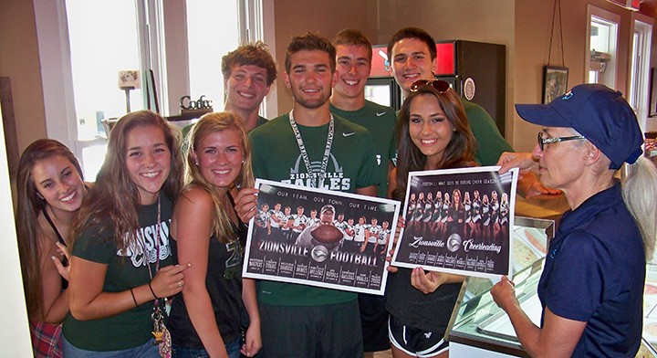 Zionsville senior football players and cheerleaders present a pair of their newly designed posters for the upcoming season to Scoops manager Monique Cunningham on July 31. Pictured, from left, are Maddie Durham, Lilli Cole, Katie Clark, Eddie Mattingly, Holden Hodge, Trevor Liechty, Scott Fuller and Grace Keller. (Photo by Sam Elliott)