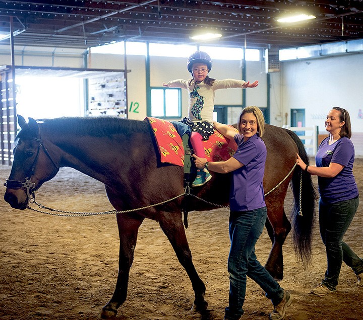 Therapy horse Rocky helps physical therapist assistant Jen Grillo work with Catalina Joyce during a physical therapy session along with horse handler Sarah Myers. (Photo by D. Todd Moore) 