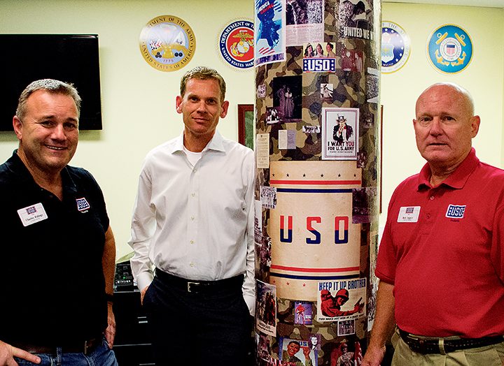 From left, Charles Ridings, Mike Hanlon and Bob Legacy converse near a pillar with advertisements for the U.S. military. Ridings is the USO of Indiana executive director and Hanlon is director of development. (Photo by Jason Conerly)