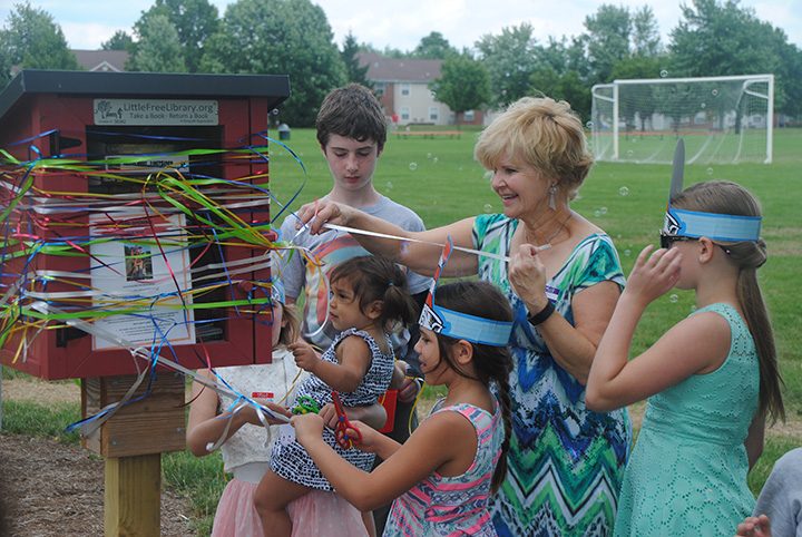Marj Sparks and a collection of eager readers perform a ribbon cutting to officially open the new Little Free Library at Holland Park. (Submitted photo)