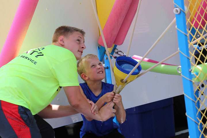 Kris Bendt, left, helps Will Doan launch a water balloon at the Water Wars game in the kids area. (Photo by Ann Marie Shambaugh)