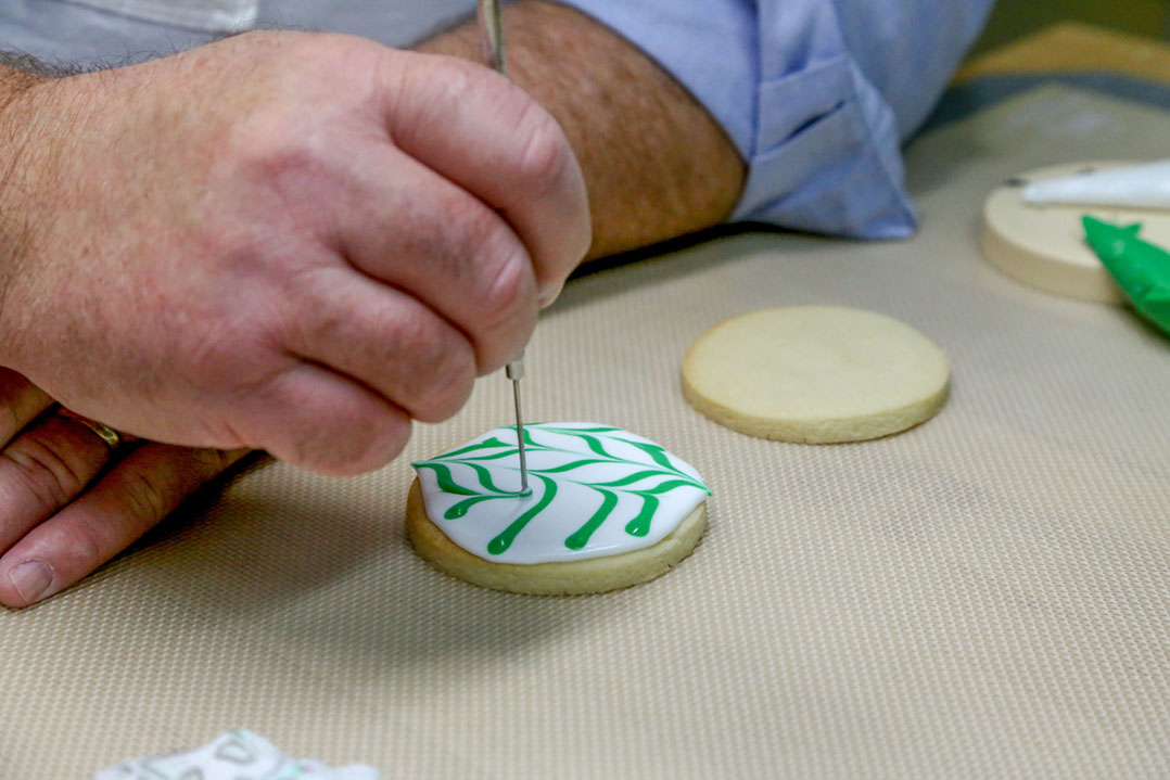 Dave Sanders of Poppy and Sweetpea’s Cookies uses a wet-on-wet technique to decorate a sugar cookie in the commercial kitchen in his Carmel home. (Photo by Ann Marie Shambaugh) 